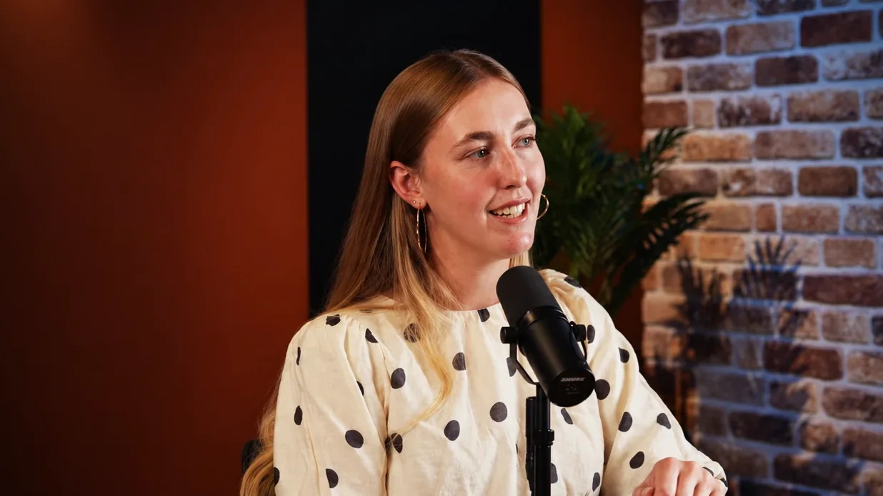Gast in een blouse met stippen lacht achter de microfoon in de studio